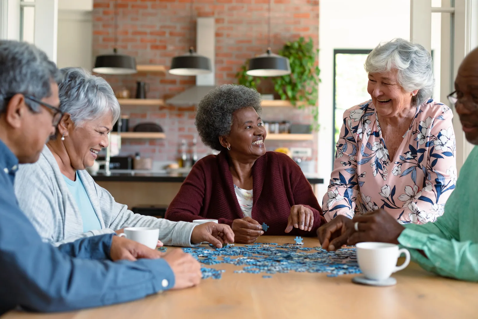 Five older adults doing a jigsaw puzzle together at a kitchen table